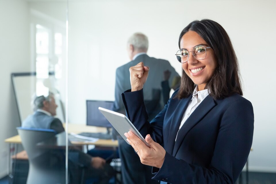 [freepicdownloader.com]-happy-female-professional-glasses-suit-holding-tablet-making-winner-gesture-